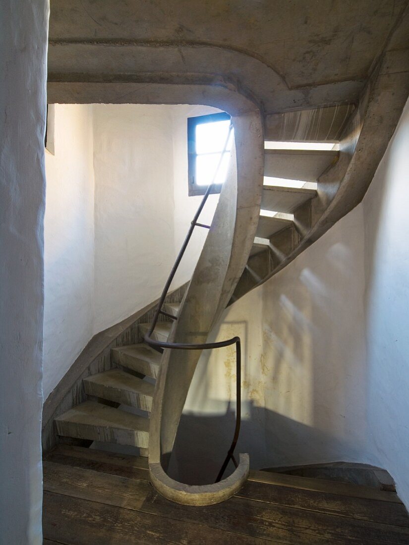 Concrete spiral staircase in renovated stairwell with patterns of light and shade