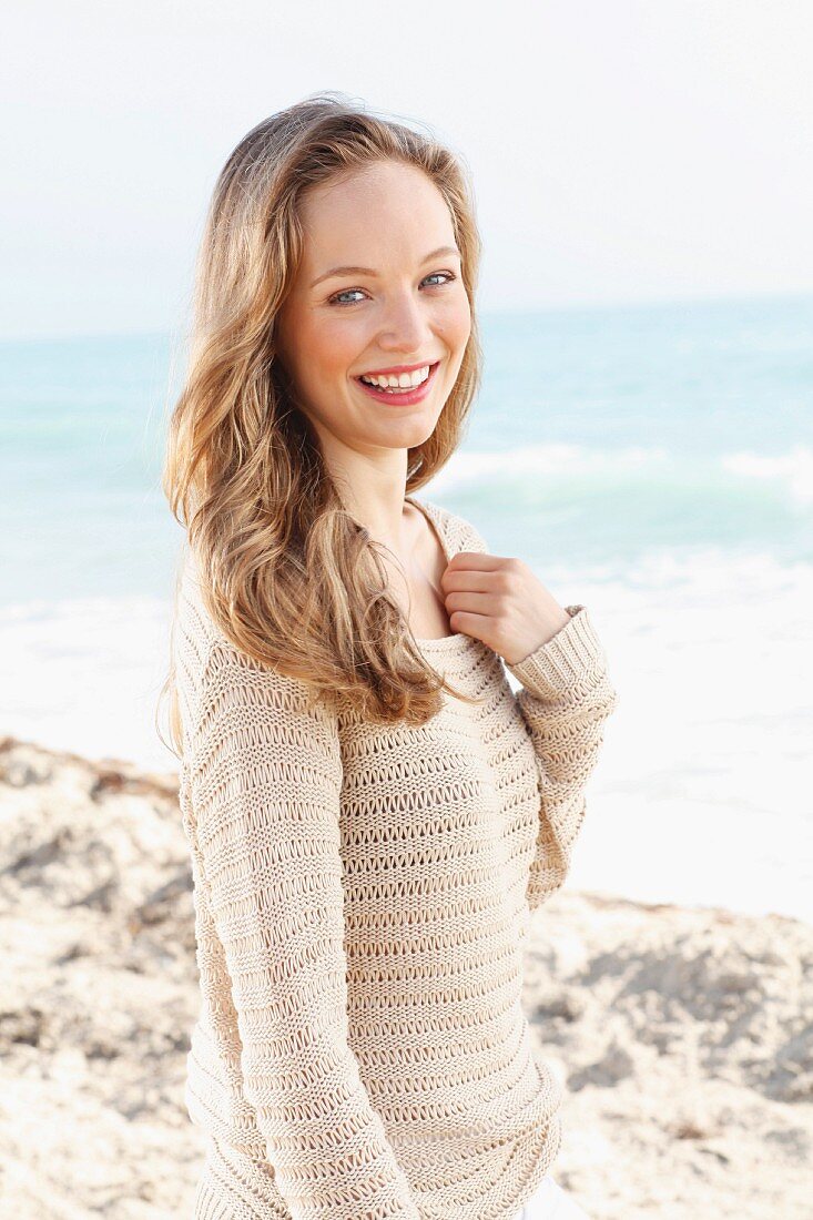 A happy young woman on a beach wearing a crocheted jumper