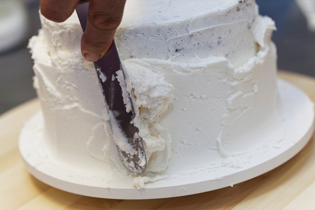 A cake being decoration with white cream