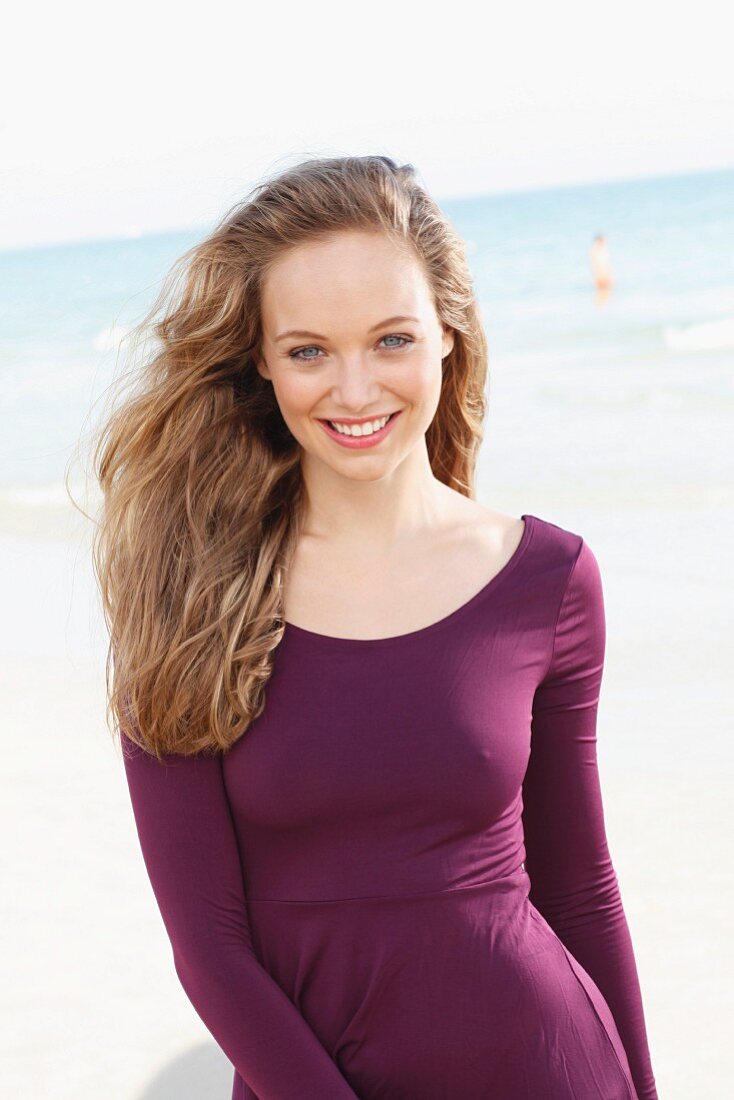 A happy yooung woman by the sea wearing a long-sleeved, purple dress