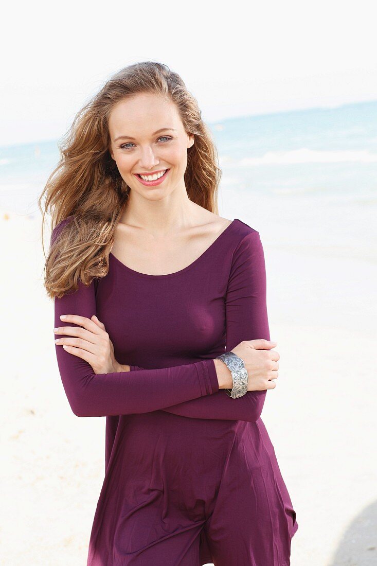 A happy young woman by the sea wearing a long-sleeved, purple dress