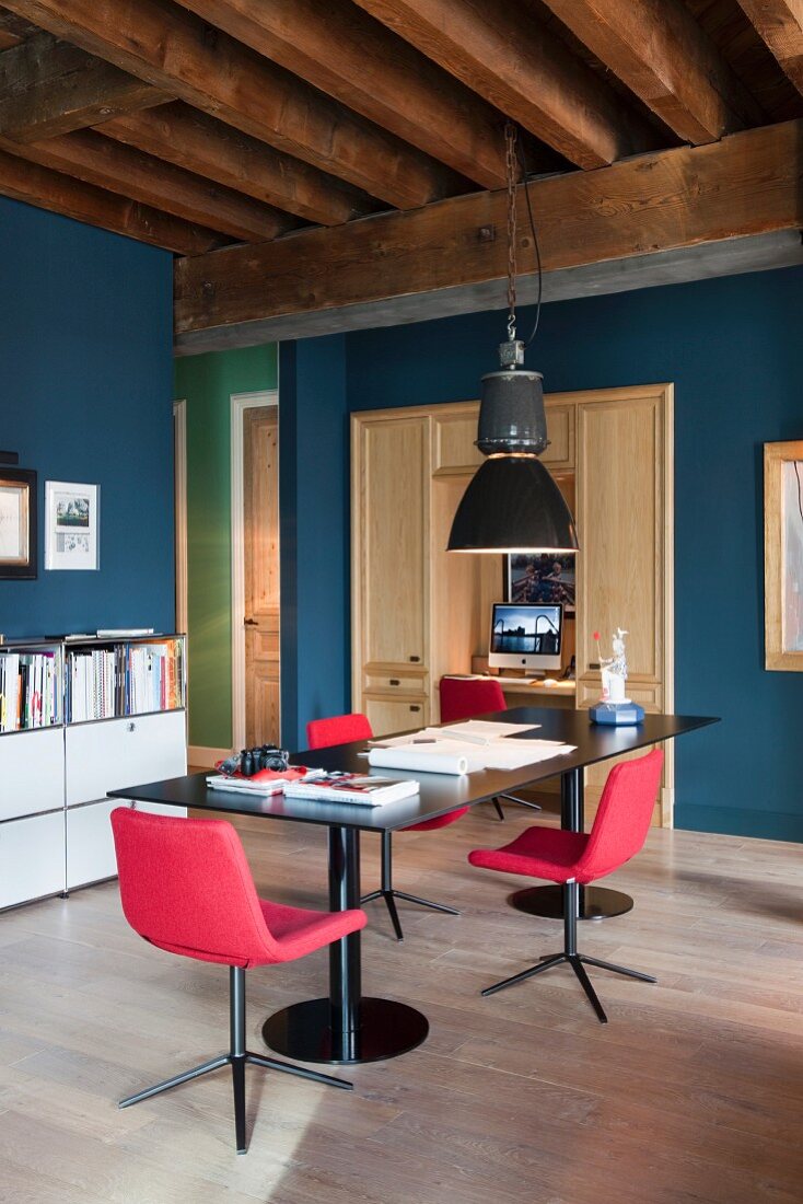 Steel table, red retro chairs and old industrial lamp as dining area and home office in open-plan, loft-apartment interior in old factory building