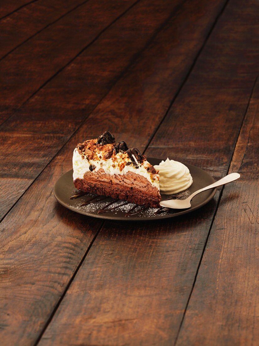 A slice of chocolate brownie cheesecake with cream