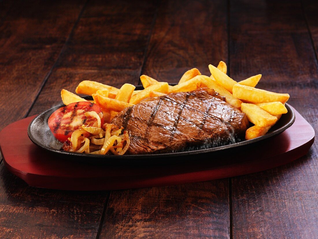 Beef steak with chips, onions and grilled tomatoes