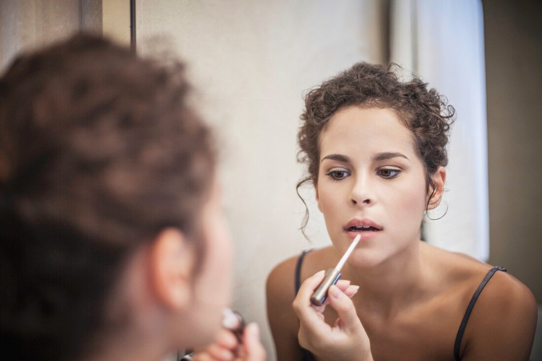 Junge Frau mit Lipgloss vor dem Badezimmerspiegel