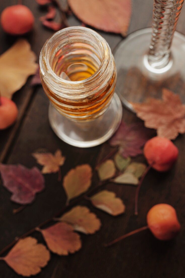 Dessertwein im Glas mit Herbstblättern und Beeren auf Holztisch