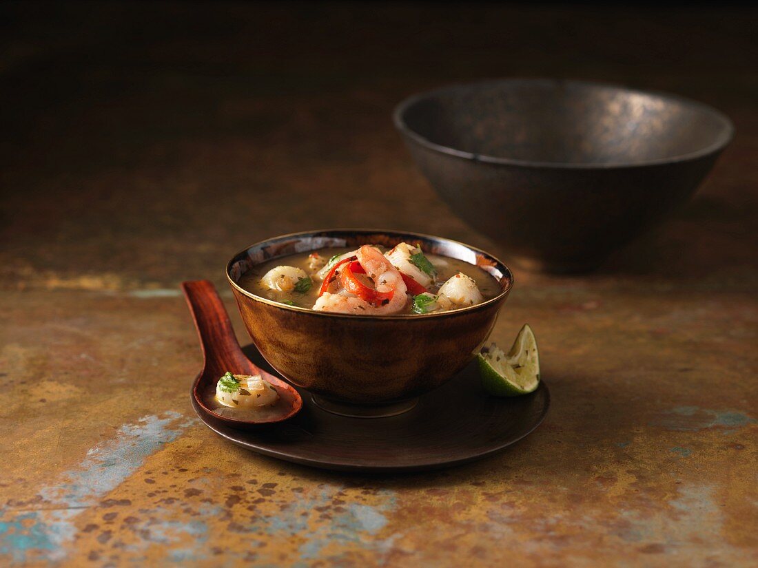 Eine Schüssel Tom Yam Suppe mit Garnelen, Chili und Limetten (Thailand)