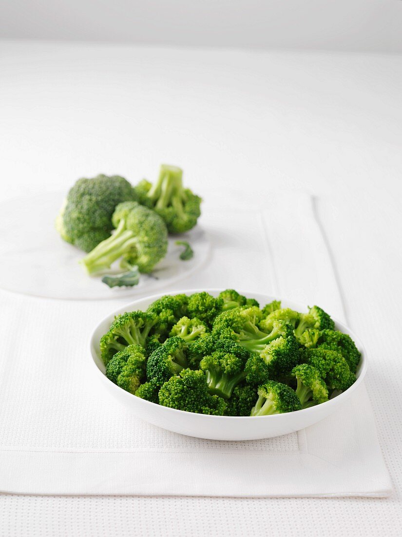 Fresh broccoli and a bowl of boiled broccoli