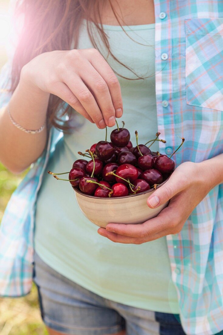 A young woman holding a bowl of cherries