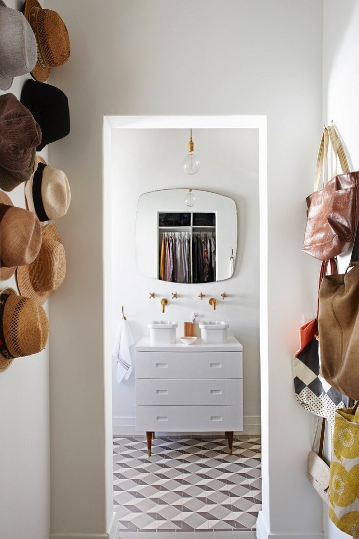 Geometric tiles, twin washstand with minimalist wall-mounted taps and retro mirror in bathroom; collection of hats and bags on wall in foreground