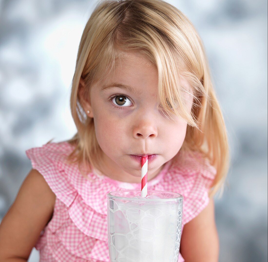 Blondes Mädchen pustet mit Strohhalm in Milchglas