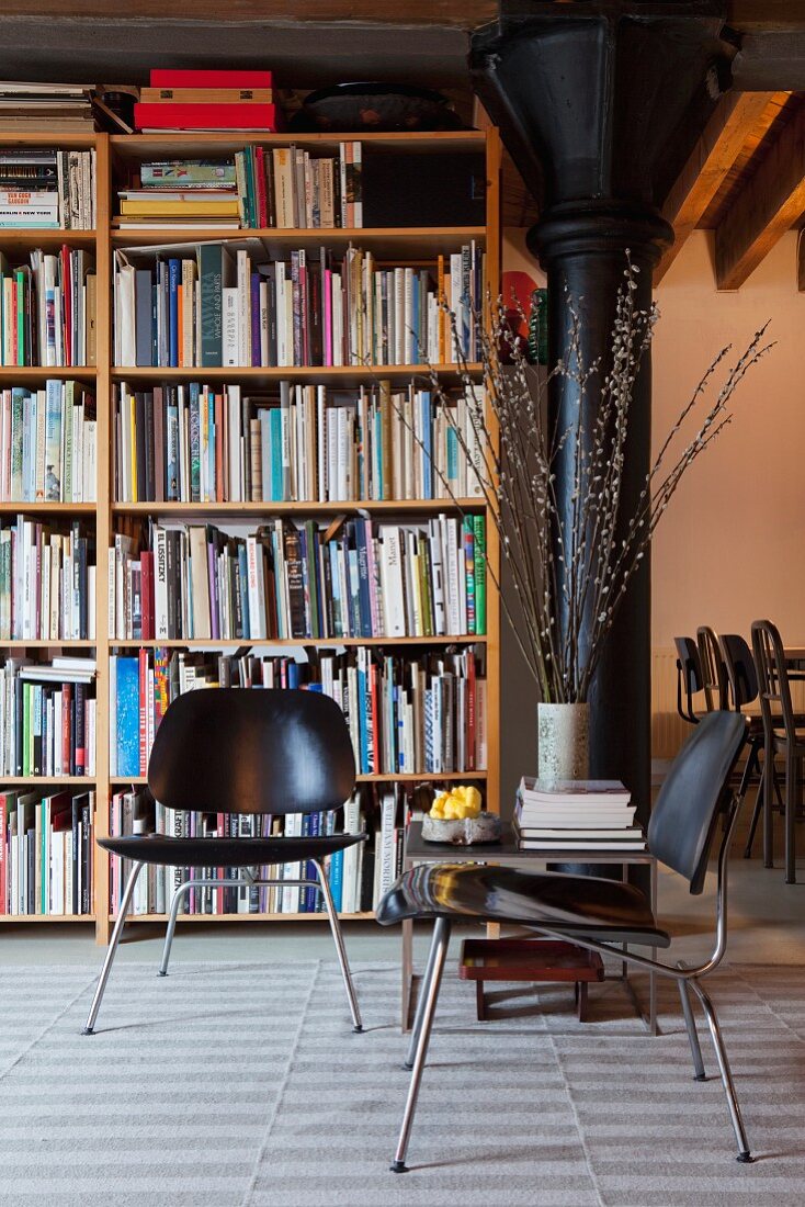 Black, retro-style chairs in front of bookcase and black metal column to one side in loft apartment