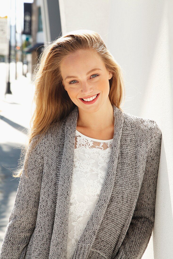 A young blonde woman wearing a white lace blouse and a grey cardigan