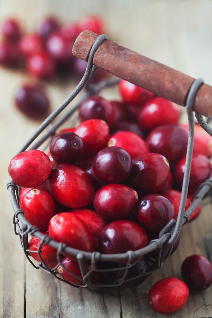 Fresh cranberries in a wire basket on a wooden surface