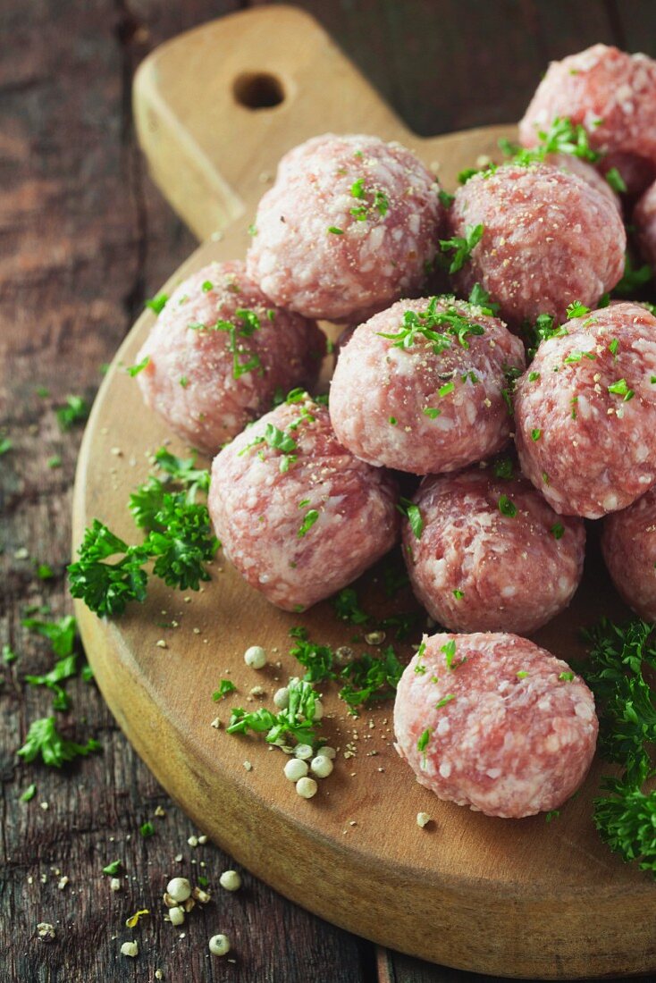Raw meatballs with parsley on a wooden surface