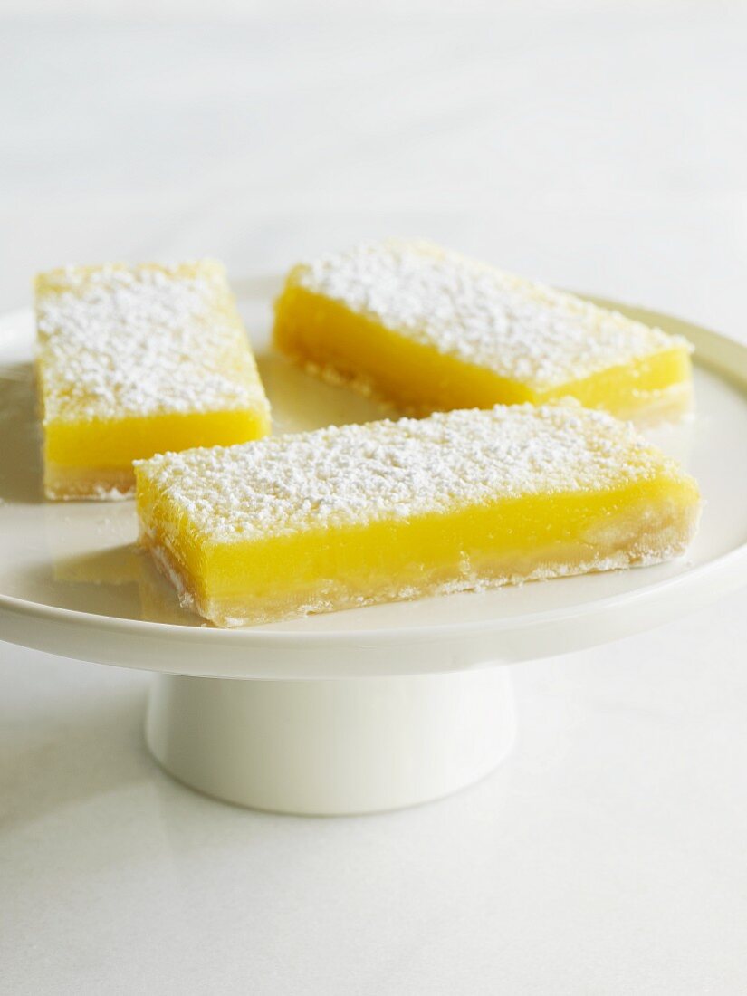 Drei Lemon Bars (ZItronenschnitten) auf einem Kuchenständer