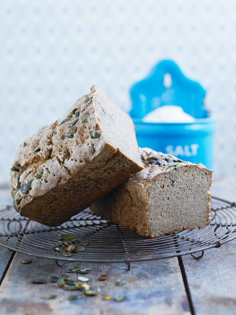 A halved bread loaf with pumpkin seeds on a cooling rack