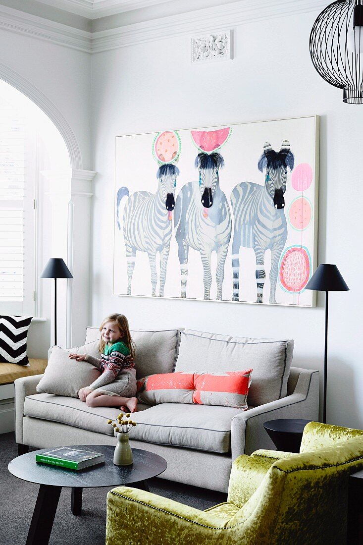 Little girl on sofa below picture of zebras and shiny gold velvet armchair