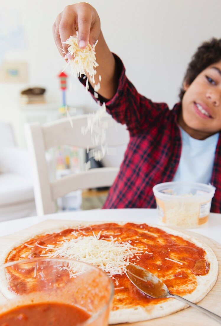 Junge streut geriebenen Käse auf eine selbstgemachte Pizza