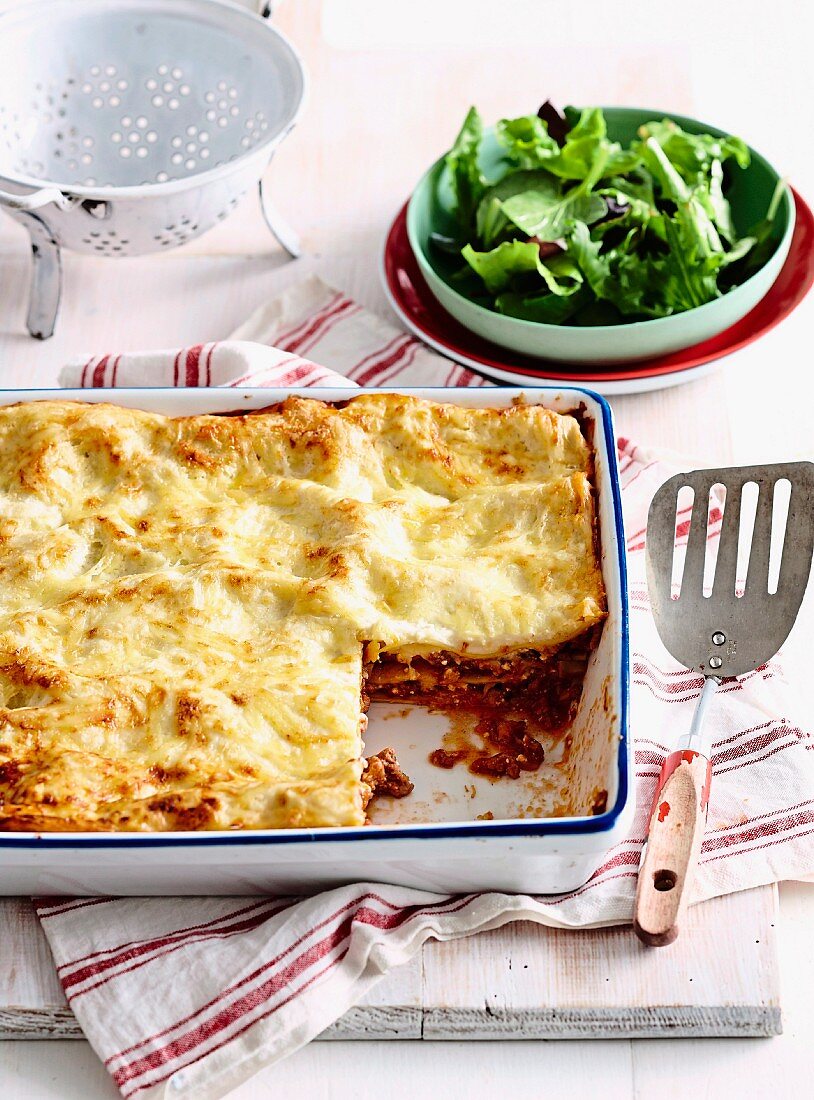 Lasagne with minced beef, mushrooms and bacon in casserole dish; served with leaf salad