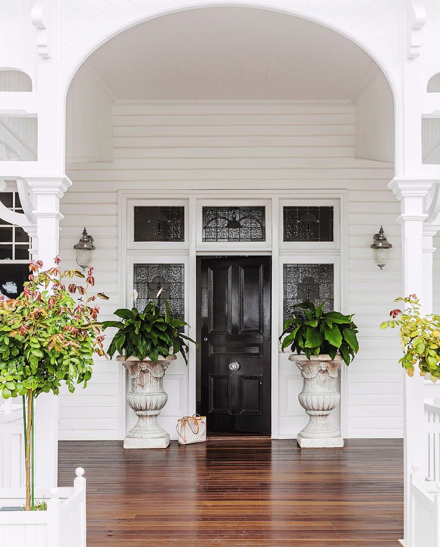 Veranda mit weiss lackiertem Torbogen und Holzboden; eleganter Hauseingang mit antiken Pflanzgefässen