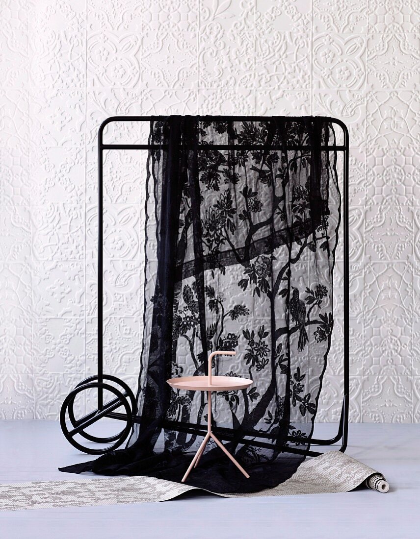 Side table and black voile cloth hanging over clothes rail against white structured wallpaper