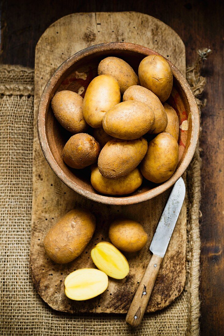 Potatoes in a wooden bowl on a chopping board with a knife