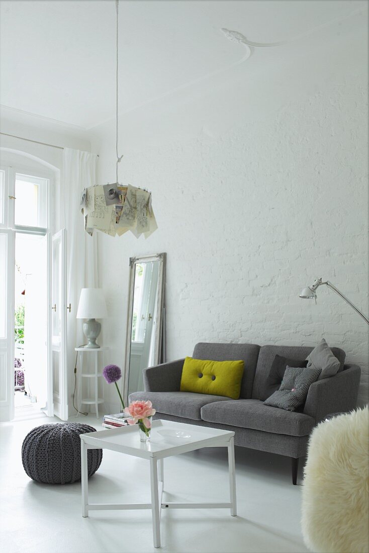 Scatter cushions on grey, retro sofa against whitewashed brick wall in interior with traditional ambiance