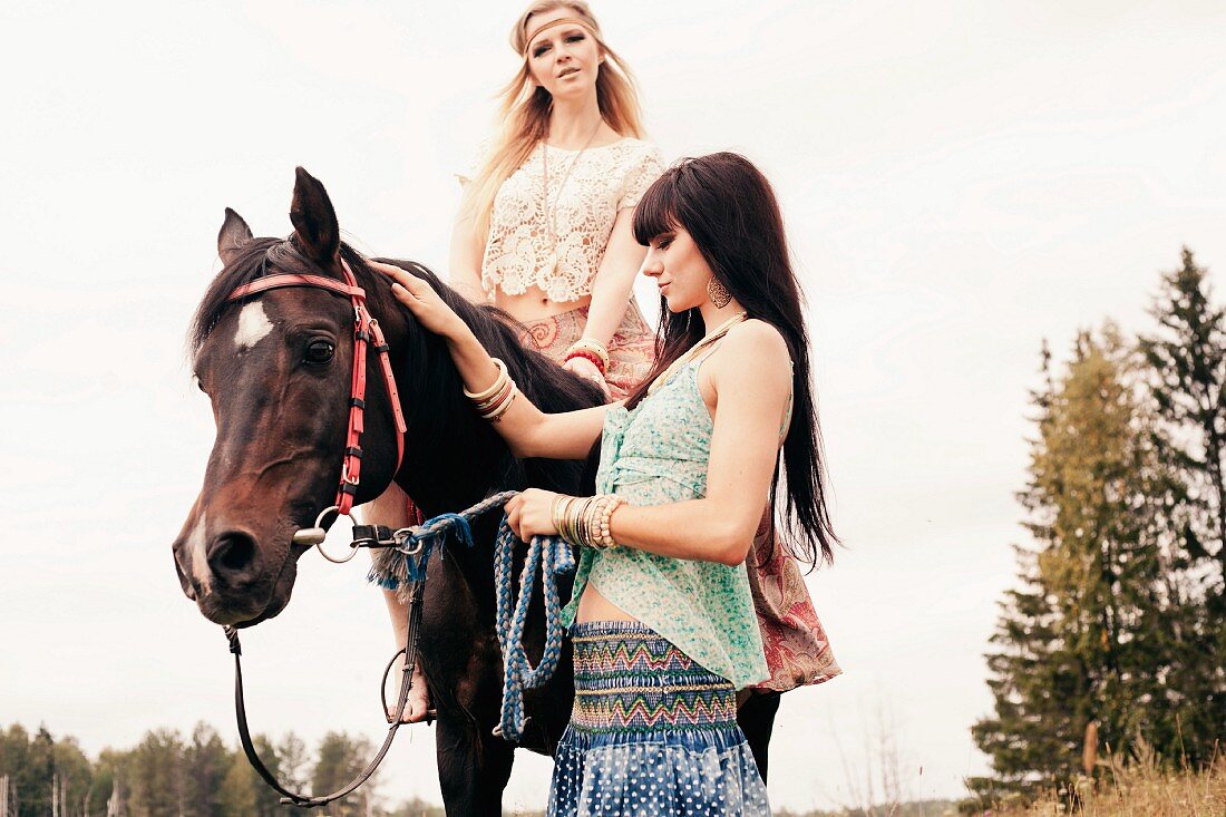 Two young women wearing hippie-style clothing with a horse