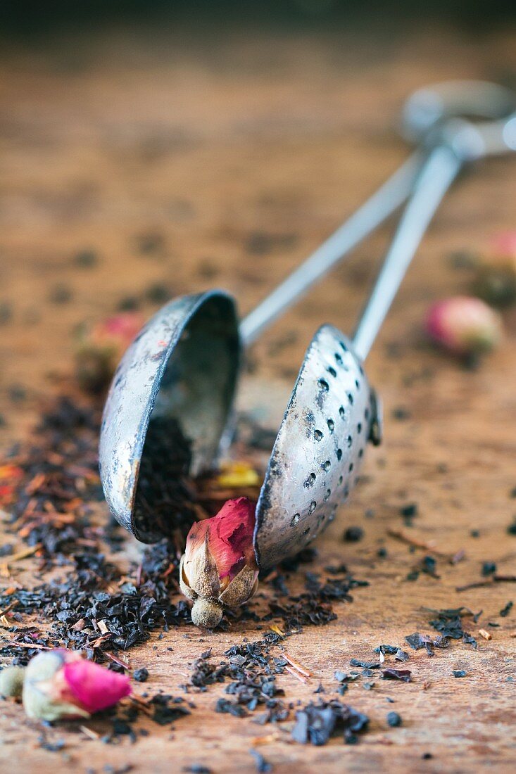 Dried tea leaves with rose buds in vintage tea strainer on a wooden surface