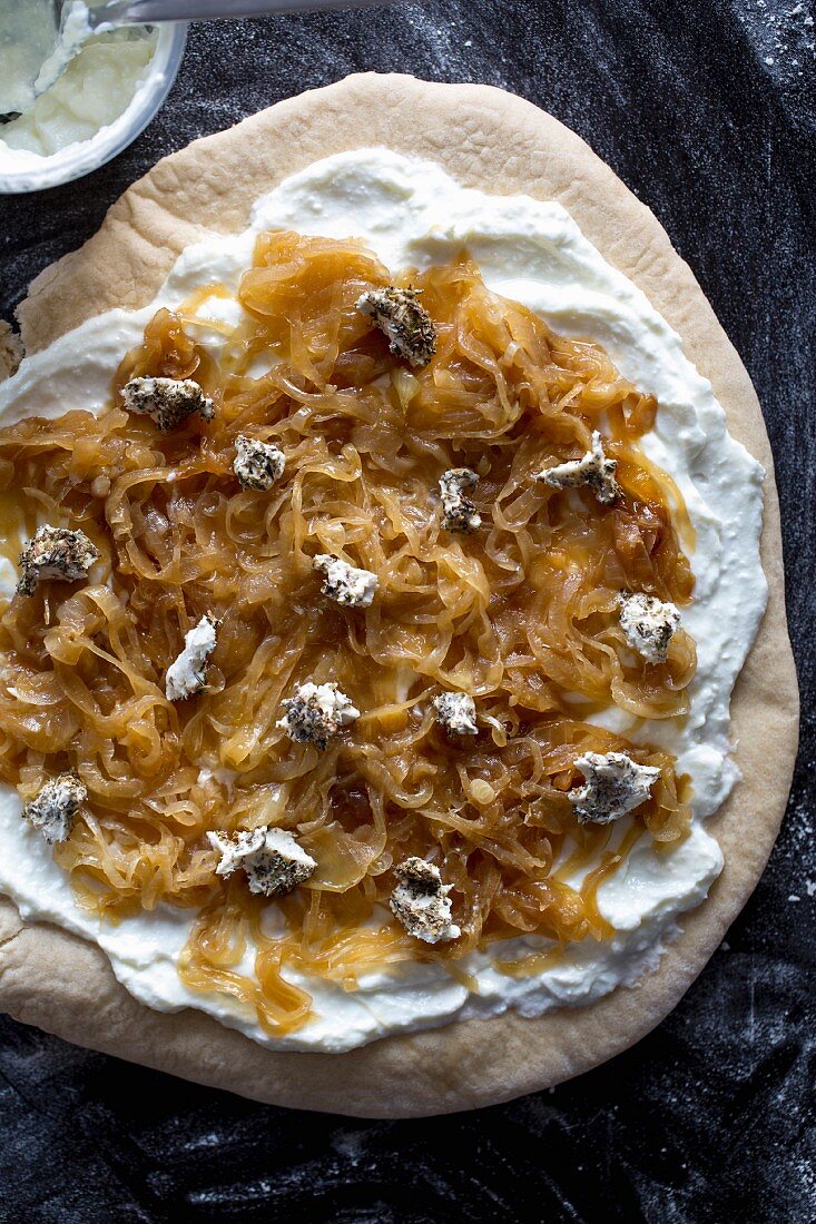 A pizza with cream cheese, caramelised onions and goat's cheese, unbaked