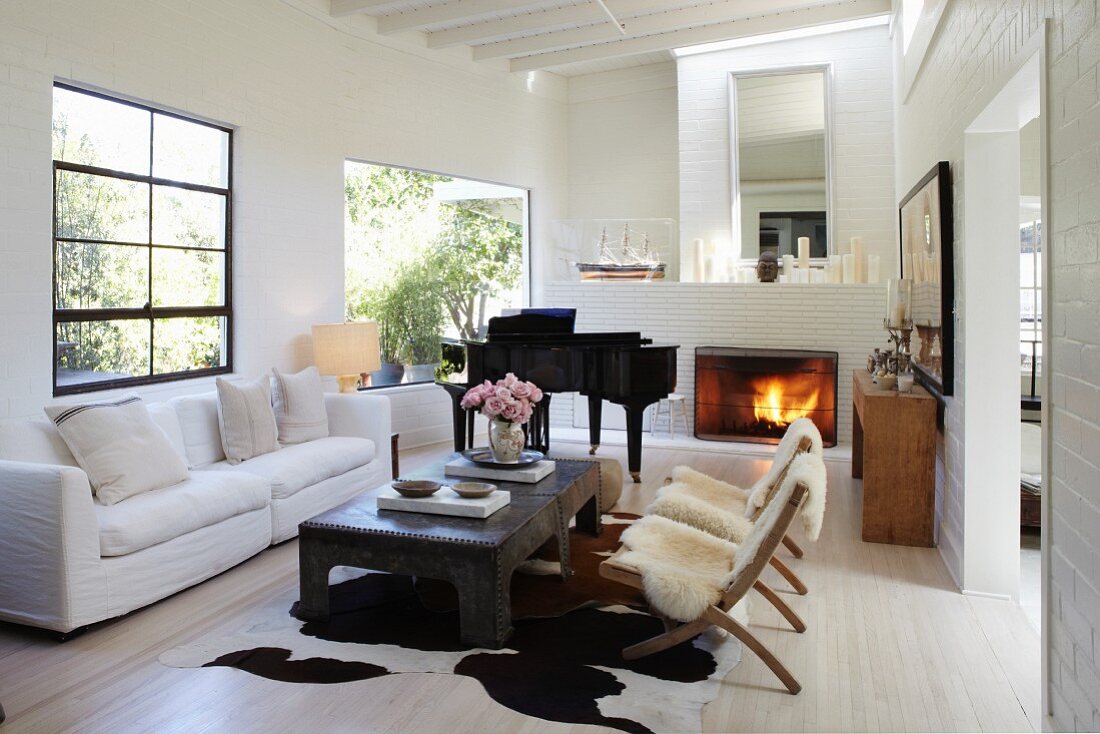 Stühle mit Tierfell und weisses Sofa um Couchtisch, im Hintergrund Klavierflügel neben Kamin im Wohnzimmer