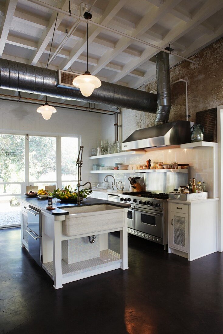 Free-standing counter in open-plan kitchen below ventilation ducts suspended from wooden ceiling