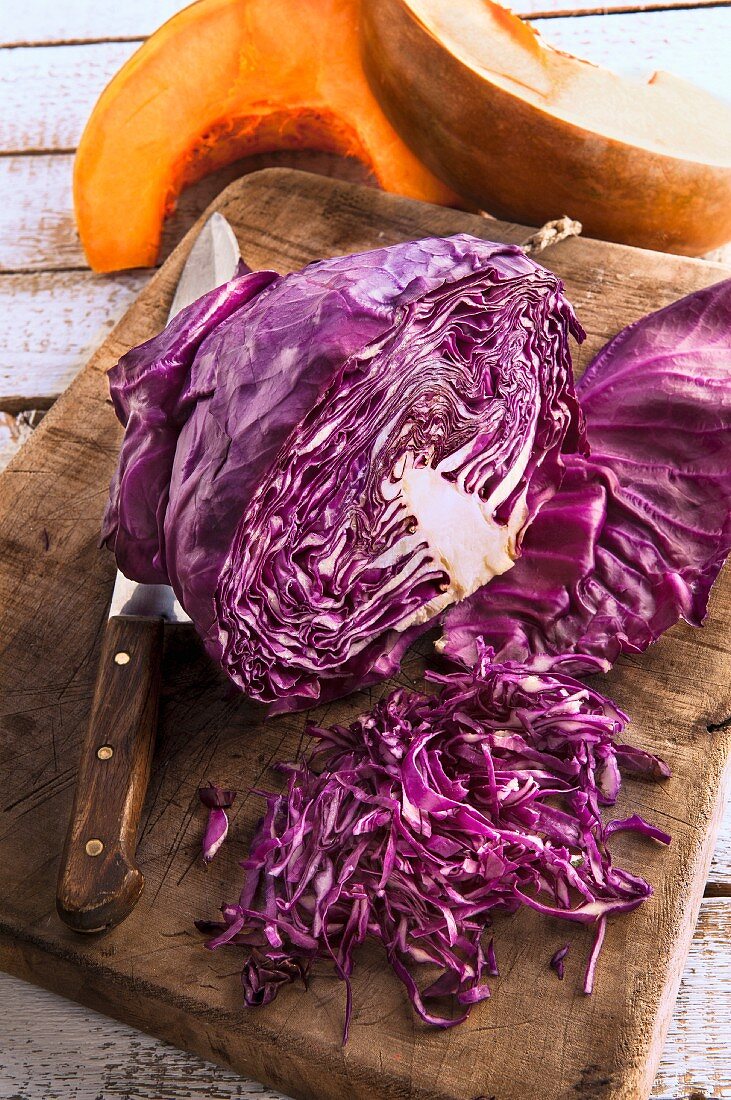 Geschnittener Rotkohl auf Schneidebrett vor Kürbisspalten