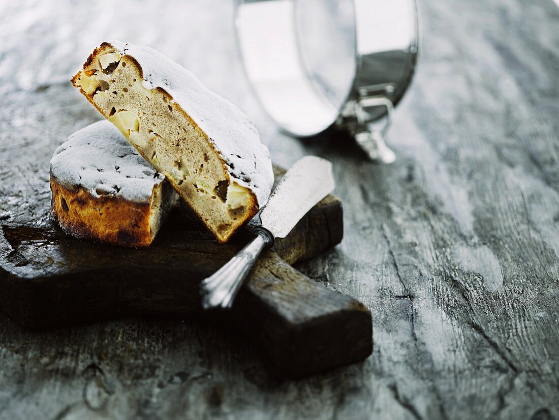 Angeschnittener, kleiner Apfel-Zimtkuchen mit Kuchenmesser auf rustikalem Holzbrett