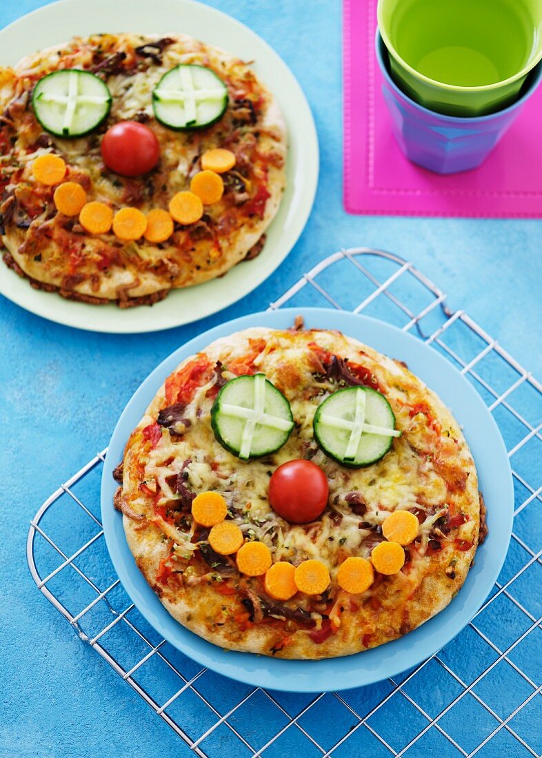 Zwei kleine Pizzen mit Gemüsegesichtern für Kinder