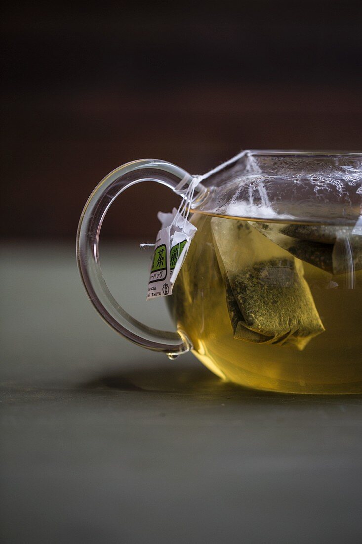 Green tea with tea bags in a glass teapot