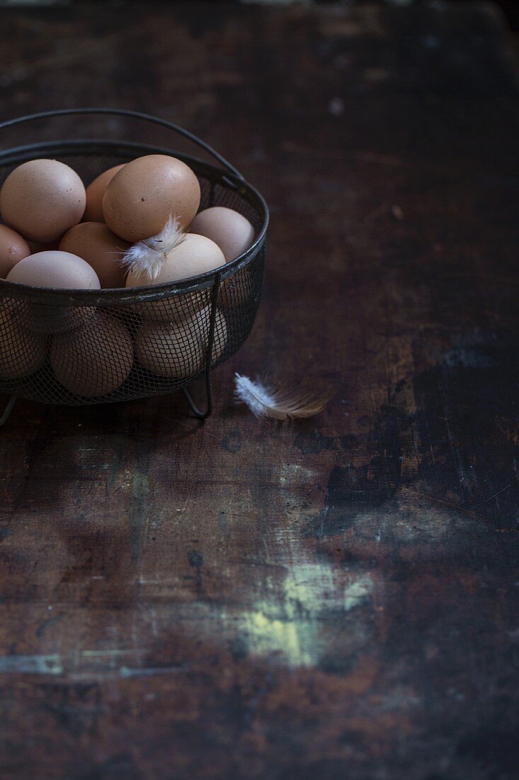 Fresh eggs in a wire basket on a wooden surface