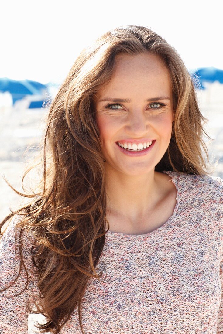 A young, long-haired woman on a beach wearing a knitted jumper