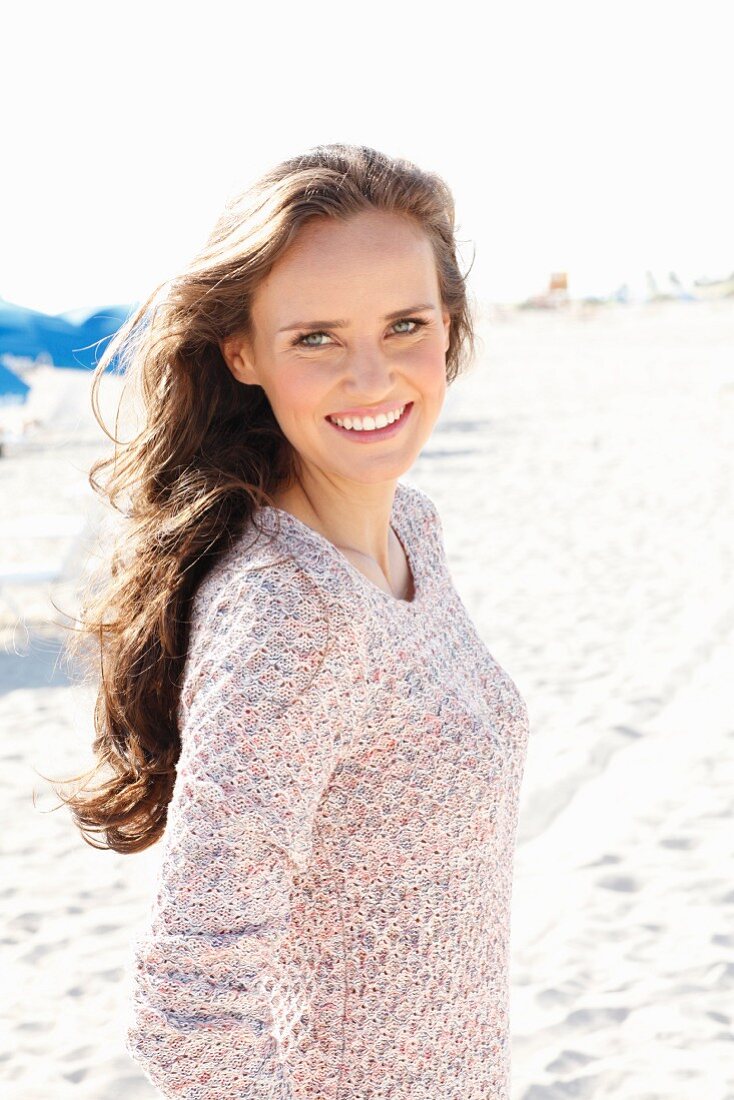 A young, long-haired woman on a beach wearing a knitted jumper