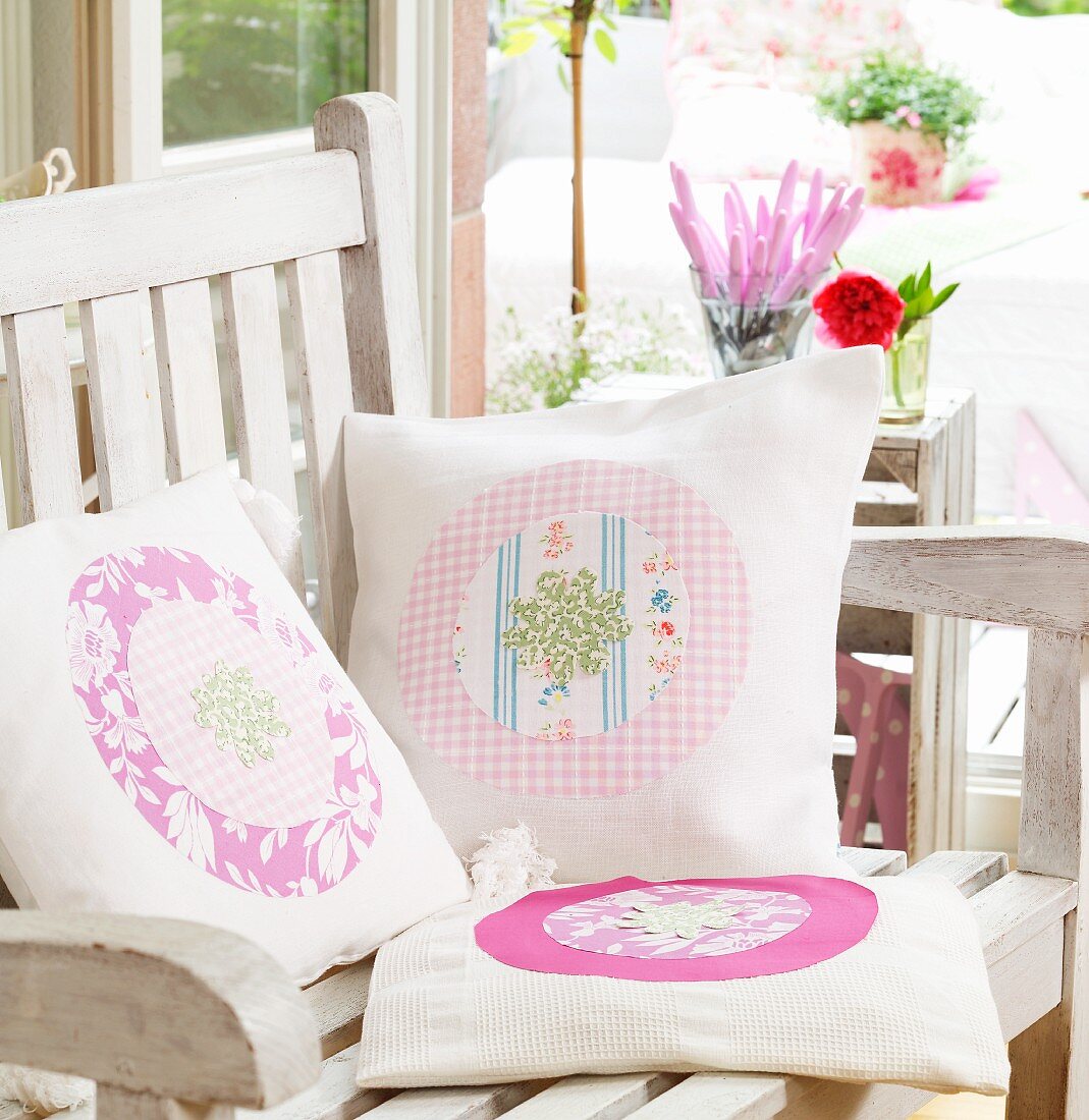 Hand-sewn scatter cushions with various patterns and appliqué motifs on wooden garden chair