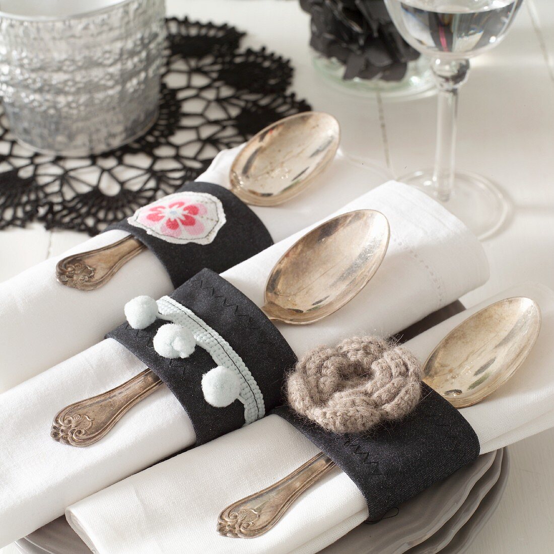 Hand-sewn napkin rings made from black fabric with appliqué flowers holding linen napkins and silver spoons