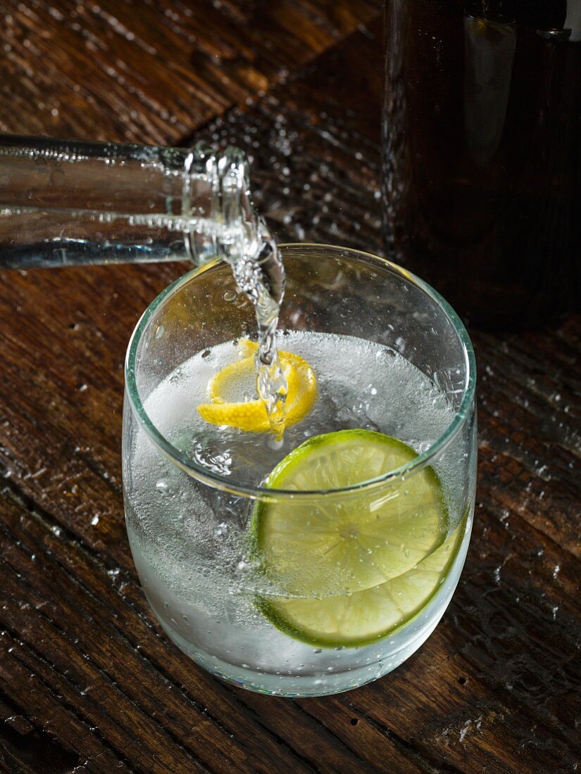 Tonic water being poured into a glass of gin