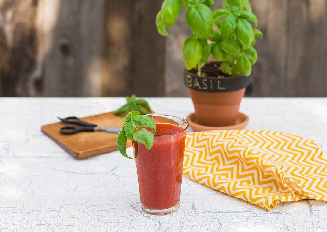 A glass of vegetable juice garnished with basil on a garden table