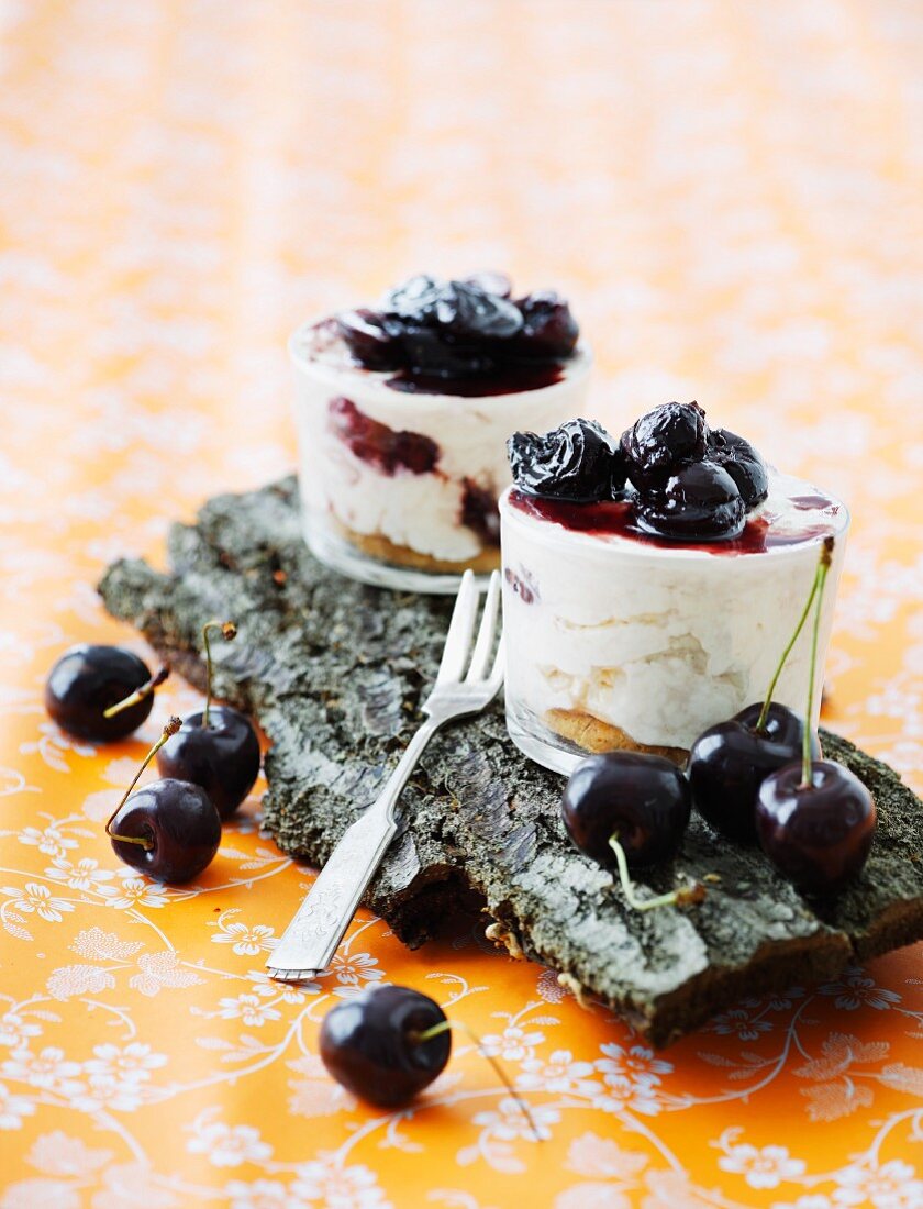 A layered dessert with cherries on a piece of bark