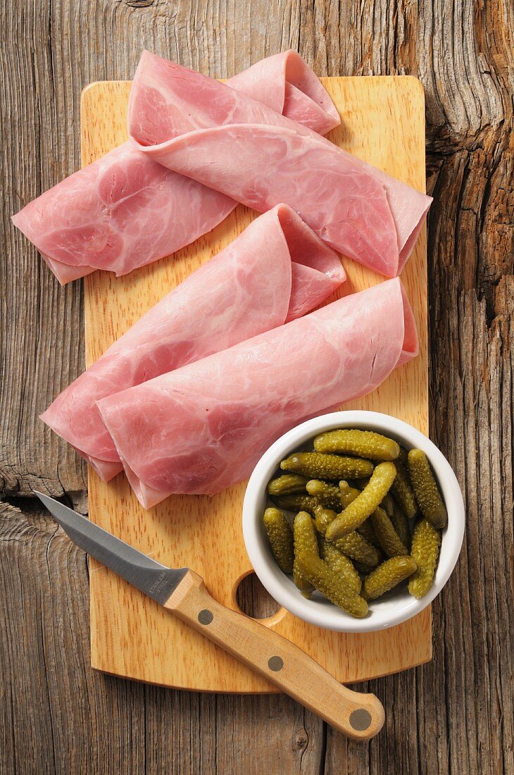 Rolled ham and gherkins on a chopping board