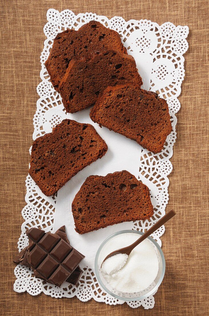 Slices of chocolate cake, sugar and pieces of chocolate on a doily