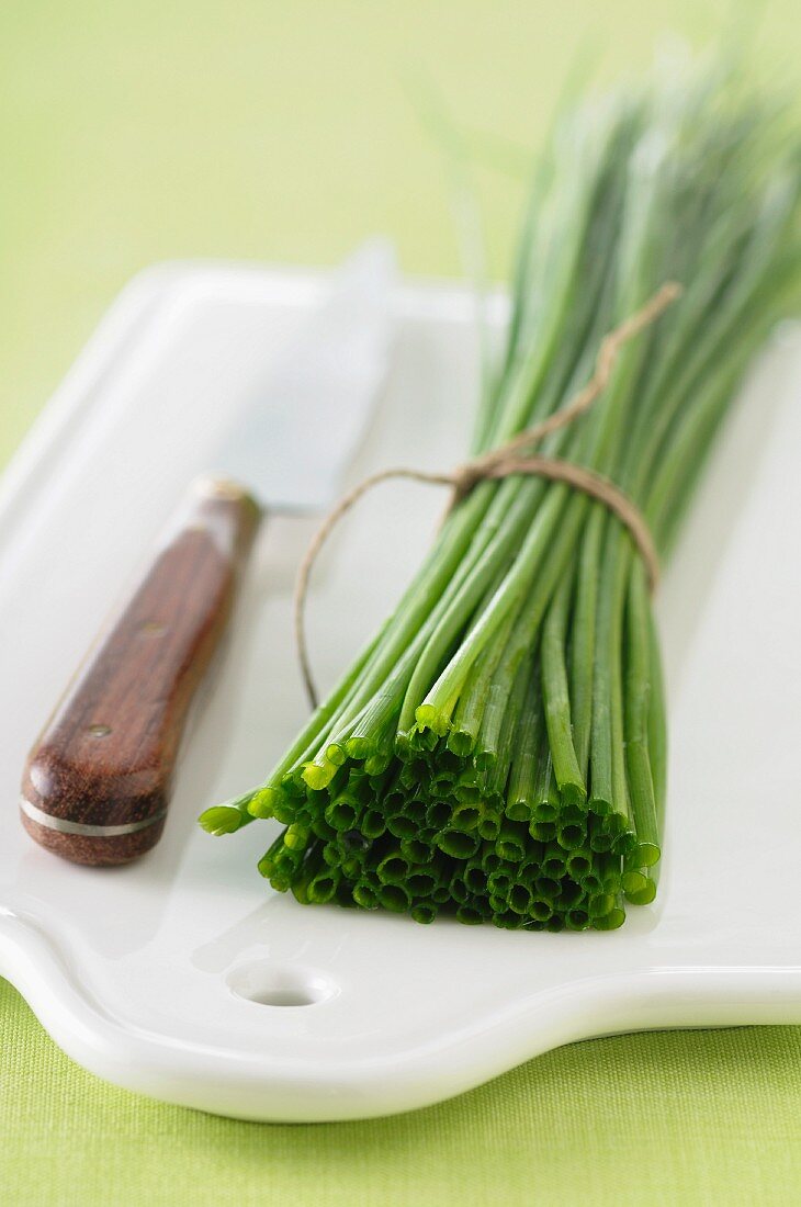 A bundle of chives and a knife on a chopping board