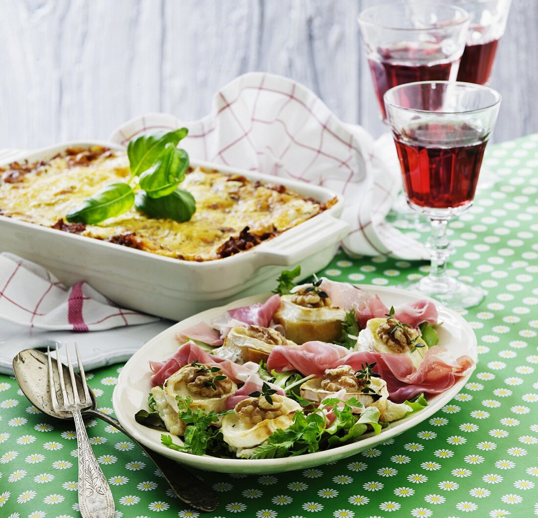 Gebackener Ziegenkäse mit Walnusskernen auf Salat mit Parmaschinken; im Hintergrund Lasagne