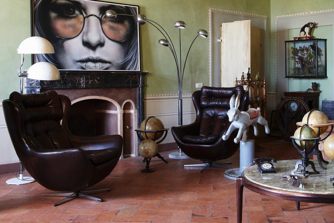 Leather bucket armchair, antique globes and vintage lamps in living room with fireplace